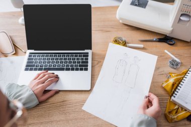 Blurred designer using laptop and holding sketches in atelier  clipart