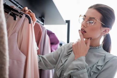 Elbiseleri askıların yanında duran düşünceli terzi. 