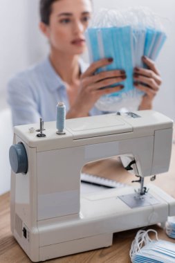 Tıbbi maske takan bulanık terzinin yanında dikiş makinesi. 