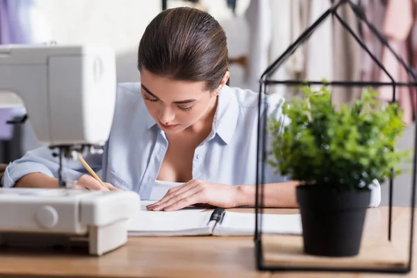 Švadlena Psaní Notebooku Blízkosti Rozmazané Rostliny Šicí Stroj Ateliéru — Stock fotografie