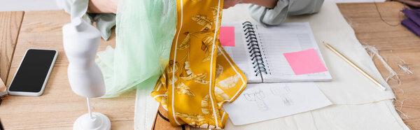 Cropped view of mannequin near sketches and seamstress with cloth, banner 