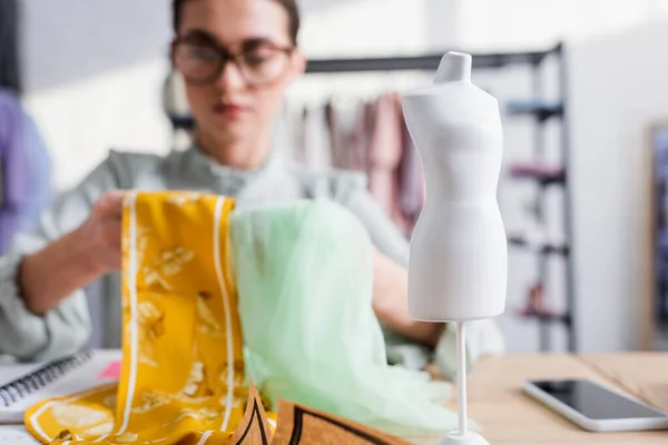 Mannequin near blurred designer with fabric in atelier