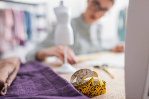 Measuring tape and fabric near blurred seamstress 
