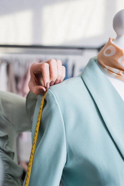 Cropped view of young seamstress with tape measure measuring jacket 
