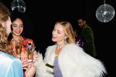 Gece kulübünde siyah arka planda içki içen çok ırklı arkadaşlar.