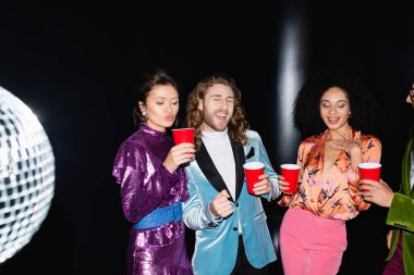 Gece kulübünde siyah arka planda dans eden mutlu çok ırklı arkadaşlar.