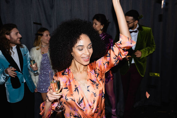 smiling african american woman dancing with interracial friends on grey background