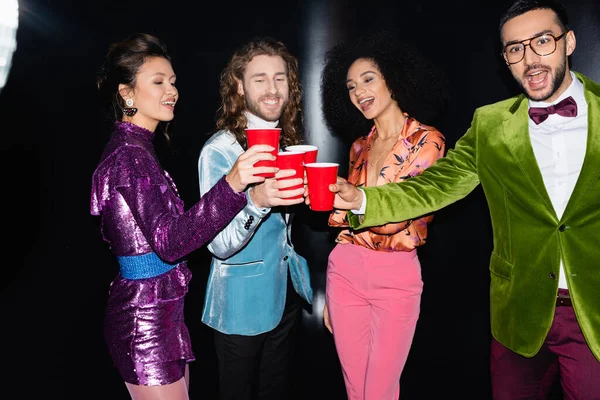 黒人を背景にナイトクラブのプラスチックカップから飲むカラフルな服の正の多人種の友人 — ストック写真
