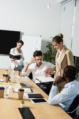 İş kadını, çok ırklı iş ortaklarının yakınındaki panoya işaret ediyor