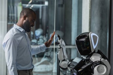 Mutlu Afro-Amerikan iş adamı robota ofiste beşlik çakıyor.