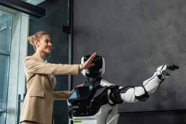 Ofiste insansı robotla el kol hareketi yapan neşeli iş kadını.