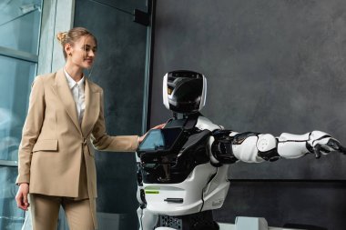 Mutlu iş kadını ofiste insansı robota dokunuyor.