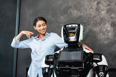 Ofisteki insansı robotu işaret eden neşeli Afrikalı Amerikalı iş kadını