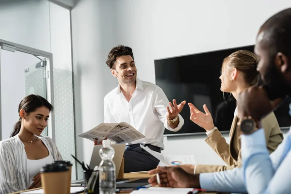 Hombre Negocios Sonriente Con Gestos Periódico Durante Reunión Con Colegas — Foto de Stock