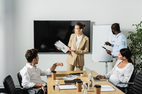 предпринимательница, демонстрирующая аналитику многонациональным коллегам во время встречи