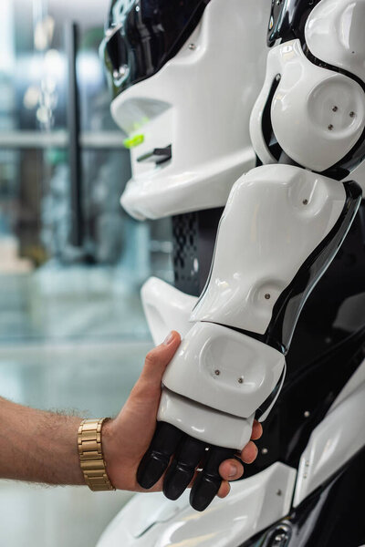 cropped view of engineer holding hand of humanoid robot