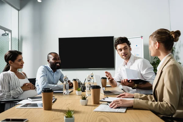 Sonriente Hombre Negocios Sosteniendo Cuaderno Mientras Habla Con Colegas Multiétnicos — Foto de Stock