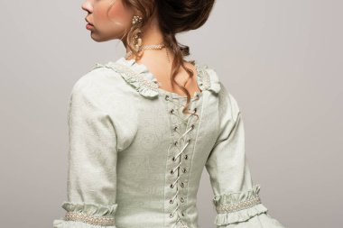 cropped view of young woman in vintage dress with lacing on back isolated on grey clipart