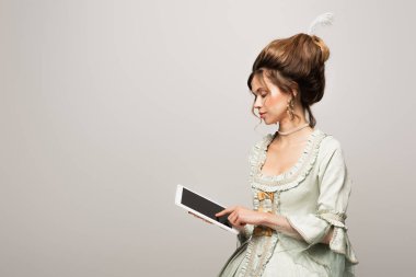 Gri ekranlı dijital tablet kullanan eski moda elbiseli genç bir kadın.