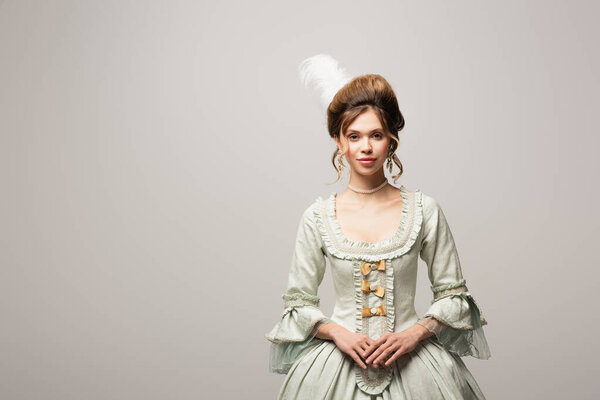 улыбающаяся женщина в элегантном винтажном платье, смотрящая на камеру, изолированную на сером