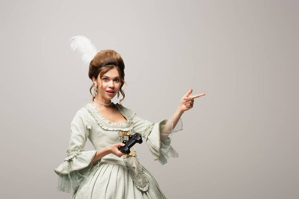 КИЕВ, УКРАИНА - 22 апреля 2021 года: удивленная, винтажный стиль женщина с джойстиком указывая прочь с пальцем изолированы на сером