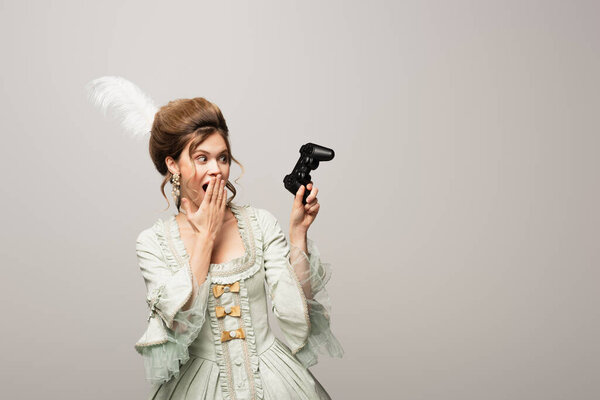 КИЕВ, УКРАИНА - 22 апреля 2021 года: шокированная женщина в стиле ретро держит джойстик и закрывает рот рукой, изолированной на сером