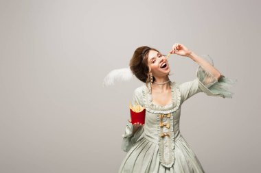 Gri renkte patates kızartması yerken kameraya bakan retro tarzı kadın.