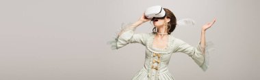 amazed woman in retro dress and vr headset gesturing isolated on grey, banner clipart
