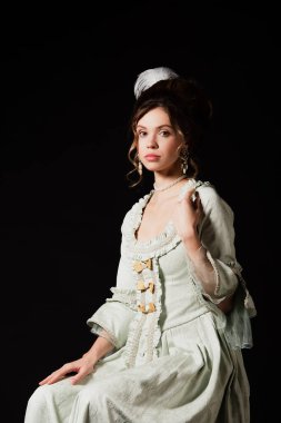 Şehvetli retro tarzı zarif elbiseli kadın siyahların üzerinde tek başına oturuyor.