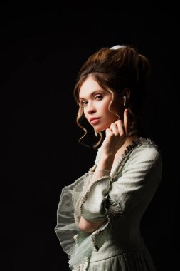 Zarif retro kıyafetli şehvetli bir kadın müzik dinliyor ve siyah kulaklığı işaret ediyor.