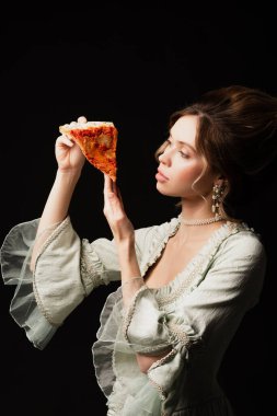Klasik kıyafetli zarif bir kadın, siyah üzerine izole edilmiş lezzetli pizzalara bakıyor.