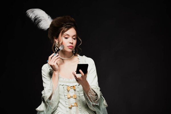 charming woman in vintage pastel grey dress applying face powder isolated on black