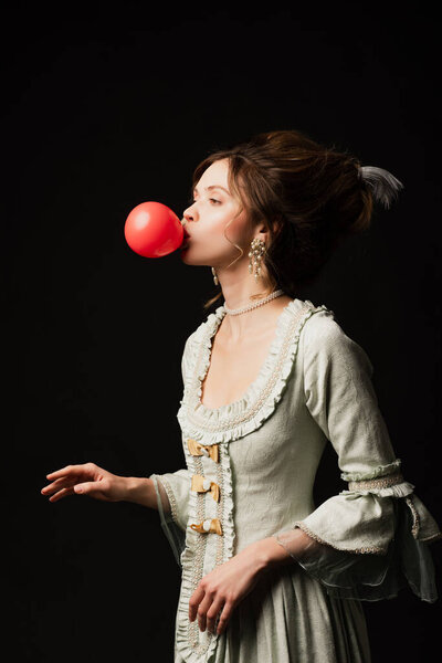 young woman in elegant vintage dress blowing chewing gum isolated on black