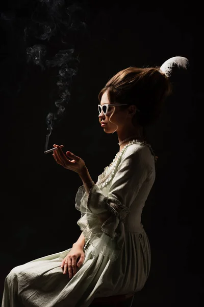 side view of vintage style woman in pastel grey dress smoking isolated on black