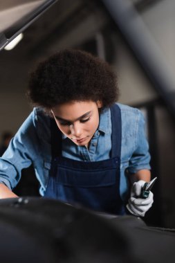Genç Afro-Amerikan tamirci kerpeten tutuyor ve garajda araba motoruyla çalışıyor. 