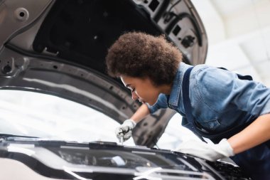 Genç Afro-Amerikan tamirci garajı açık kapüşonlu bir arabada motor tamir ediyor.