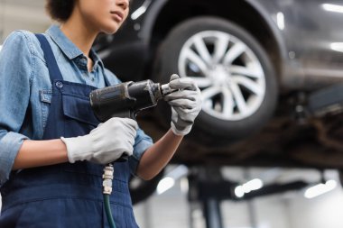 Oto tamir servisinde elektrikli tornavida tutan elleri eldivenli genç tamircinin kısmi görüntüsü