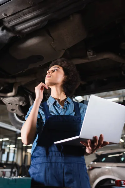 Young African American Mechanic Inspecting Lifted Car Laptop Hand Garage — Stock Photo, Image