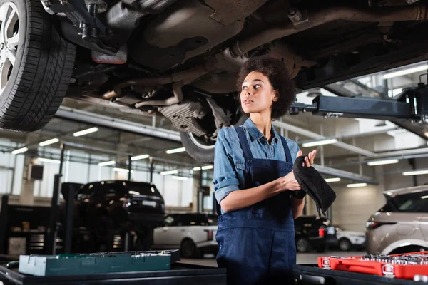 Joven Afroamericano Mecánico Overoles Pie Debajo Del Coche Secado Manos — Foto de Stock