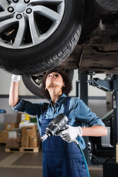 Young African American Mechanic Overalls Repairing Wheel Lifted Car Electric — Stock Photo, Image