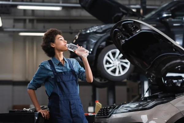 Young African American Mechanic Overalls Drinking Water Plastic Bottle Car — Stock Photo, Image