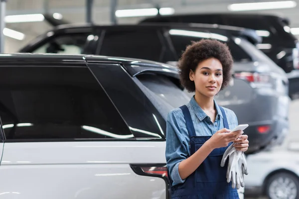 正の若いアフリカ系アメリカ人の整備士が自動車修理サービスのスマートフォンに立ち — ストック写真