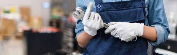 cropped view of young mechanic with hands in gloves holding wrench in auto repair service, banner