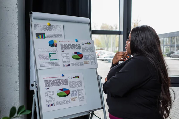 african american plus size businesswoman looking at flip chart with charts and graphs