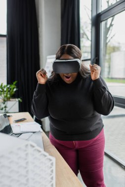 Şaşırmış Afrikalı Amerikalı artı boyut mühendisi vr kulaklık içinde bulanık ev modelinin yanında 