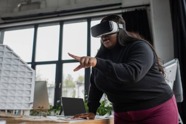 Şaşırtıcı Afrikalı Amerikalı artı VR kulaklıklı mühendis karton ev modelini işaret ediyor. 