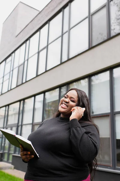 Sorridente Afro Americano Size Mulher Segurando Notebook Falando Smartphone Fora — Fotografia de Stock