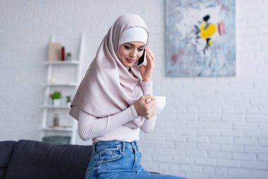 Gülümseyen Arap kadın cep telefonuyla konuşurken elinde çay fincanı tutuyor.