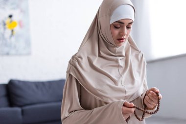 Tespihi olan genç müslüman kadın evde gözleri kapalı dua ediyor.