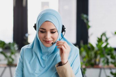 Çağrı merkezinde çalışan kulaklıklı, pozitif Müslüman kadın.
